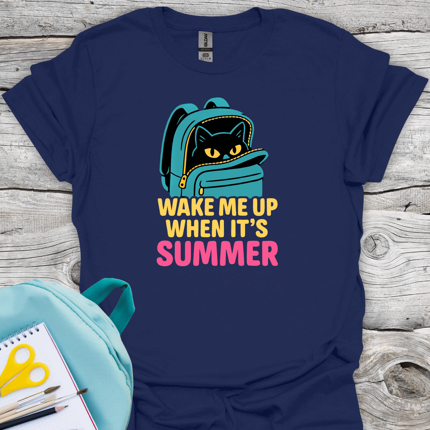 Navy blue t-shirt with a cat in a backpack graphic and 'Wake Me Up When It's Summer' text on a wooden surface.